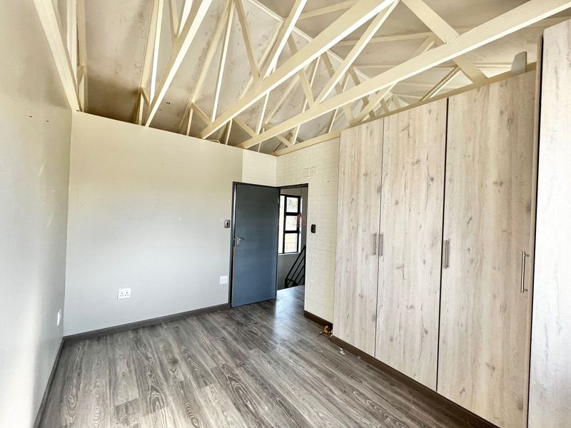 An empty bedroom featuring laminate flooring, built-in cupboards, and exposed roof trusses, offering a blank canvas for renovation or interior design.