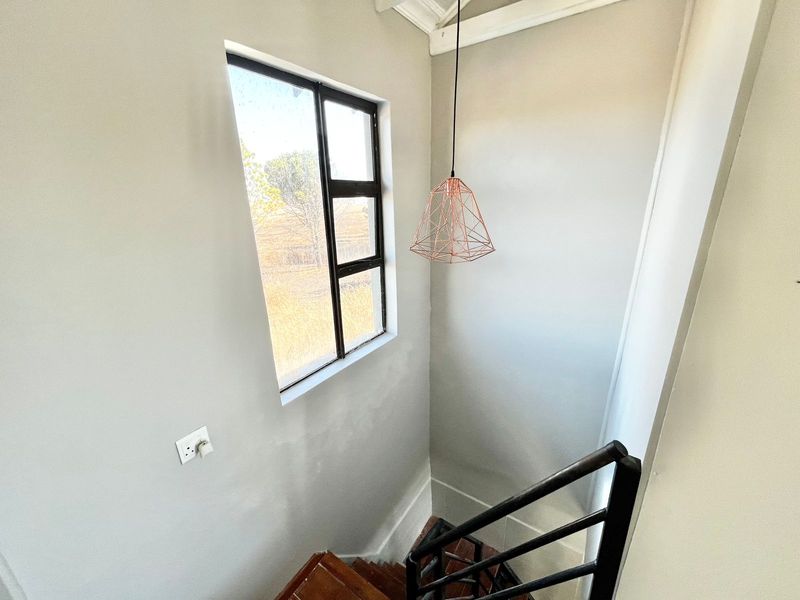 A bright staircase landing featuring a modern pendant light, metal handrail, and a window providing natural light.