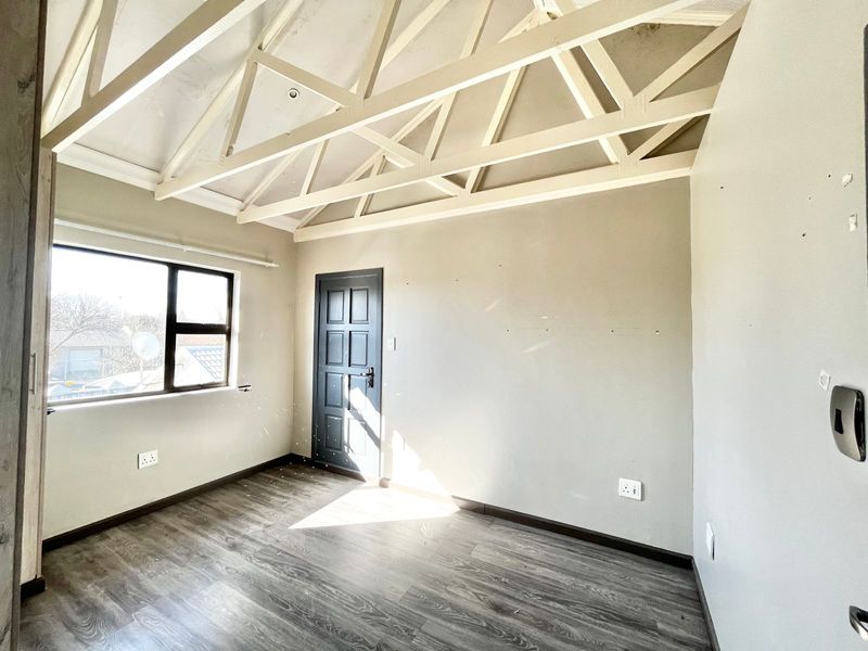 A bright, empty bedroom featuring exposed white roof trusses, modern laminate flooring, and a dark panelled door, offering a clean canvas for interior design.
