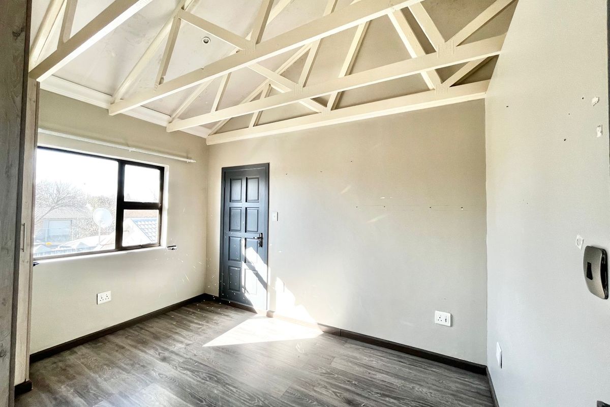 A bright, empty bedroom featuring exposed white roof trusses, modern laminate flooring, and a dark panelled door, offering a clean canvas for interior design.