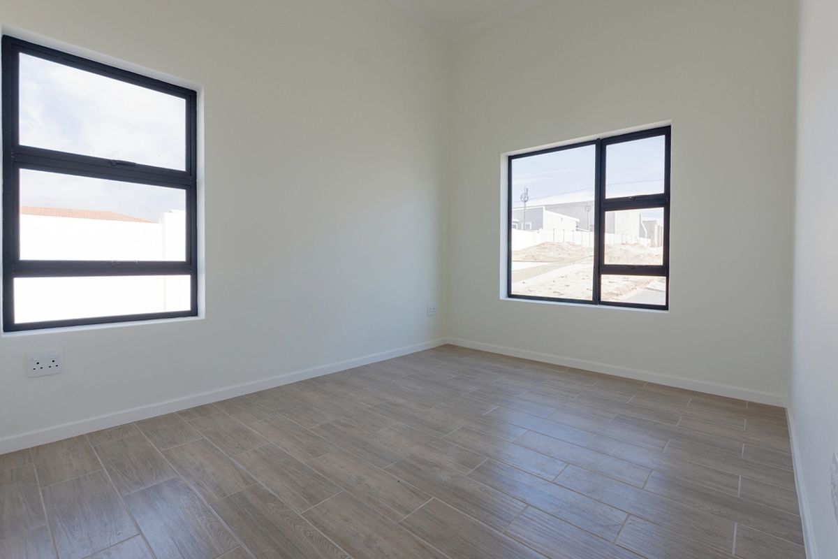 A bright, empty bedroom featuring modern wood-look floor tiles and large aluminium-framed windows, providing a clean and neutral canvas for interior design.