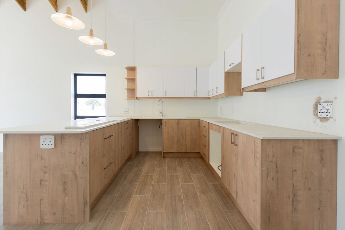 Modern kitchen featuring light wood-tone cabinetry, stone countertops, tiled flooring, and exposed timber beams. The space is clean and ready for final appliance installation.