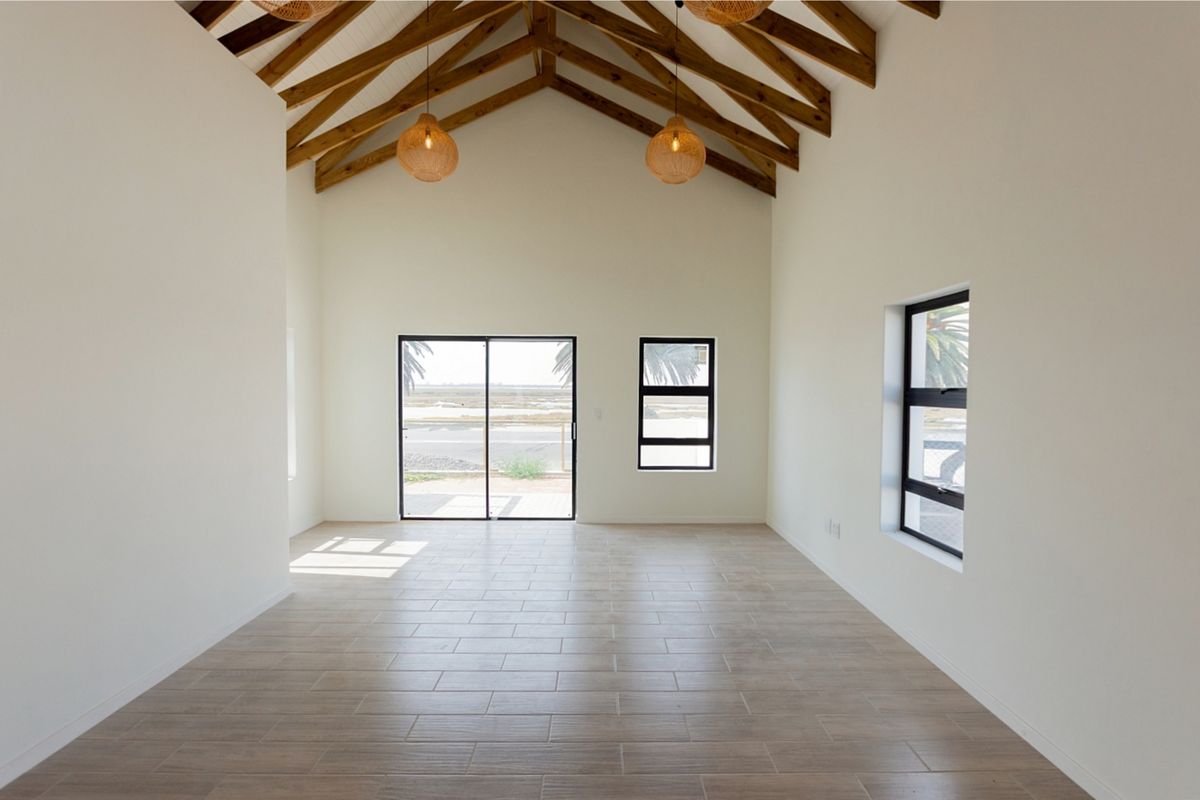 Spacious living area featuring a high vaulted ceiling with exposed timber trusses, tiled flooring, and large windows providing natural light and outdoor views.