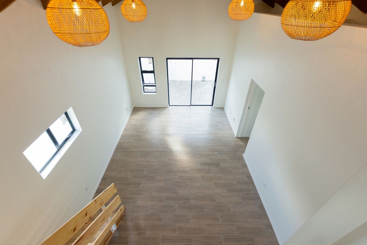 Spacious, light-filled living area featuring high ceilings with exposed timber rafters, modern tiled flooring, and large sliding glass doors leading to the exterior.