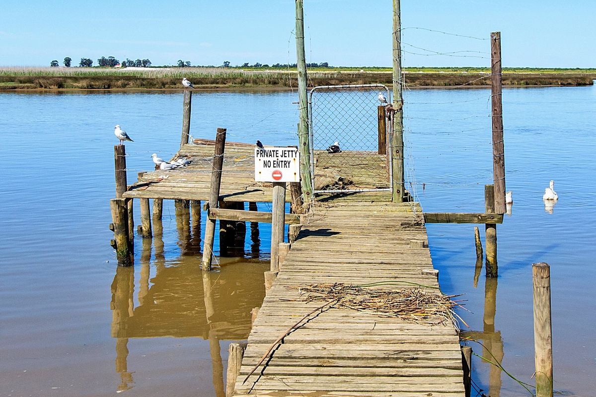 A weathered wooden jetty extending into the water, featuring a gated entrance and timber structural supports.