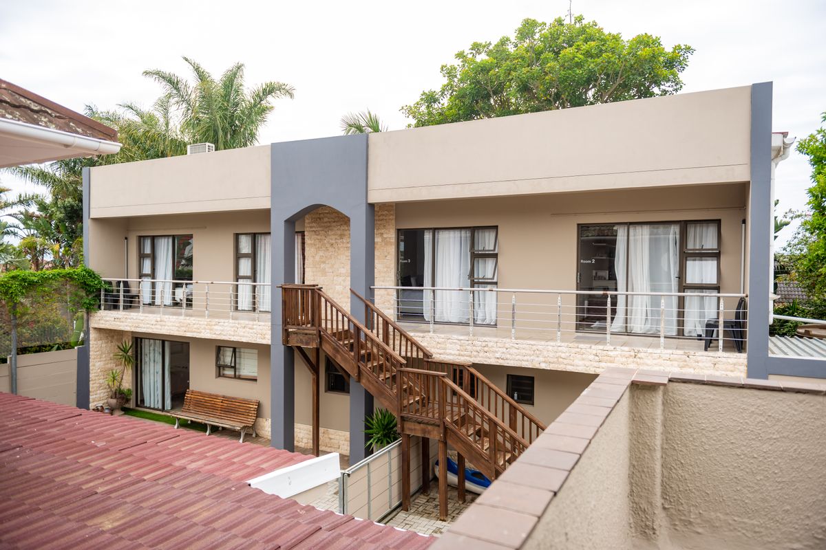Rear exterior view of a two-story building featuring a timber staircase, stone cladding accents, and sliding glass doors leading to upper and lower levels.