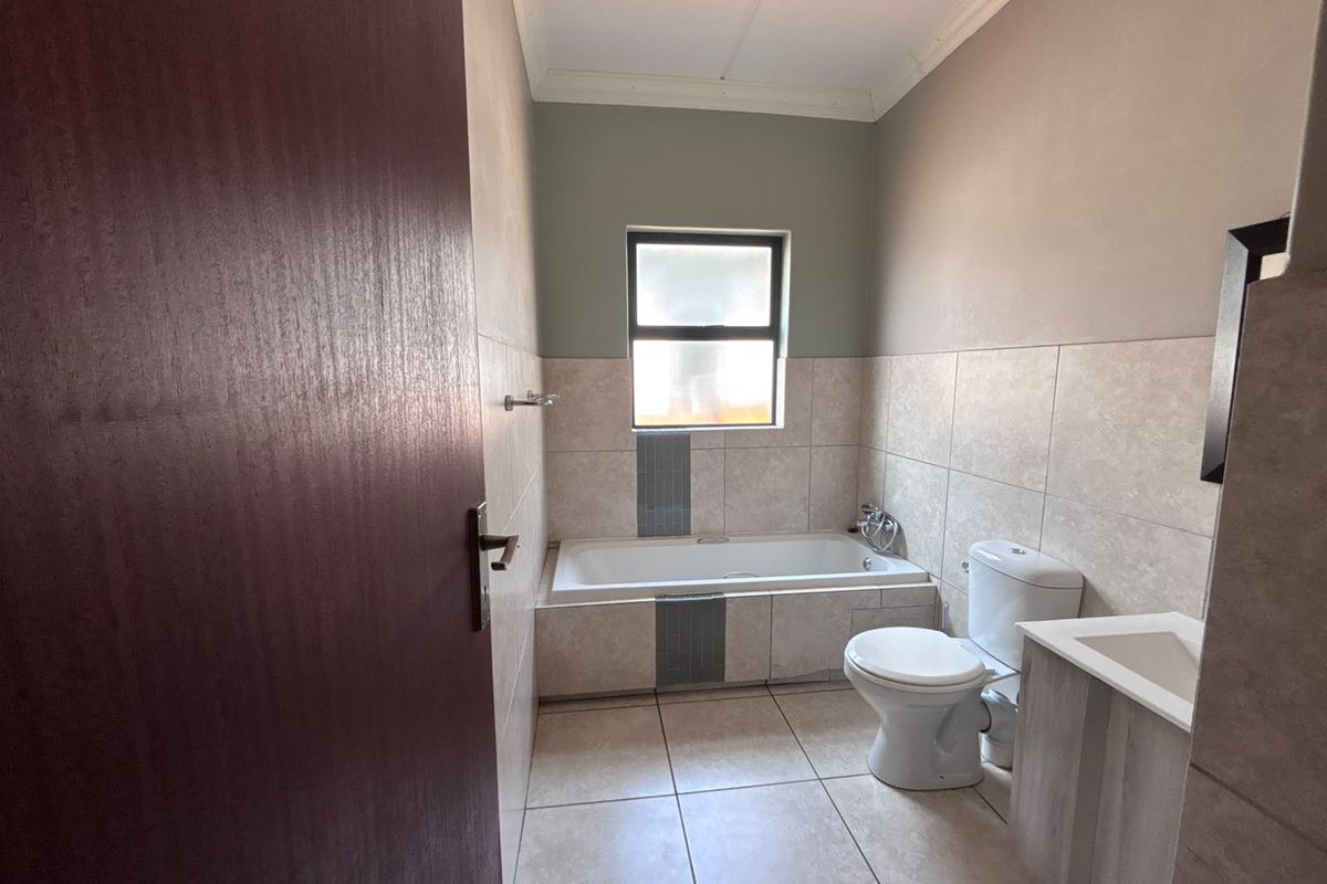 A clean and functional bathroom featuring a built-in bathtub, toilet, and vanity cabinet with neutral tiled finishes throughout.