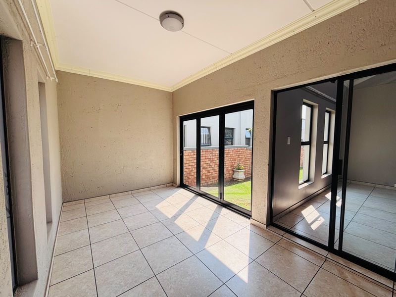 A bright, empty enclosed patio featuring tiled flooring and large sliding glass doors that provide access to the outdoor area.