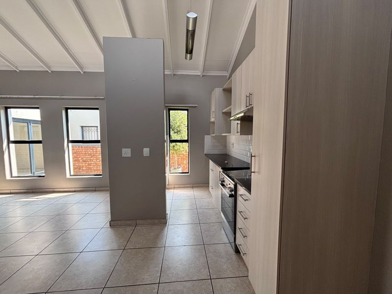 Open-plan living and kitchen area featuring tiled floors, exposed beam ceilings, and modern built-in cabinetry with integrated appliances.