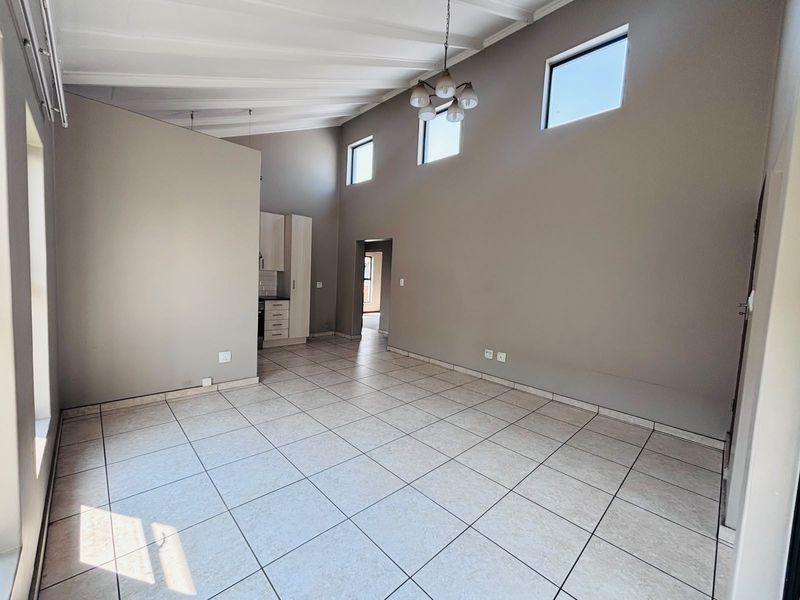 Spacious open-plan living area featuring vaulted ceilings with exposed beams, neutral tiled flooring, and high-level windows providing ample natural light.