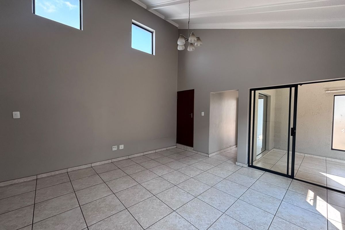 Spacious living area featuring vaulted ceilings, neutral tiled flooring, and large sliding glass doors that provide access to the outdoor space.