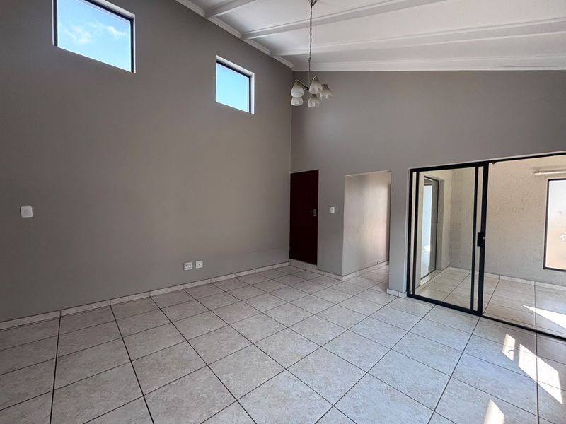 Spacious living area featuring vaulted ceilings, neutral tiled flooring, and large sliding glass doors that provide access to the outdoor space.