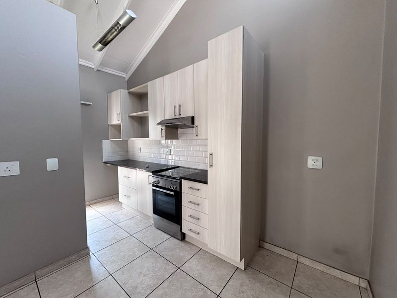 A clean, modern kitchen featuring light wood-finish cabinetry, a subway tile backsplash, built-in electric stove with extractor, and vaulted ceilings.