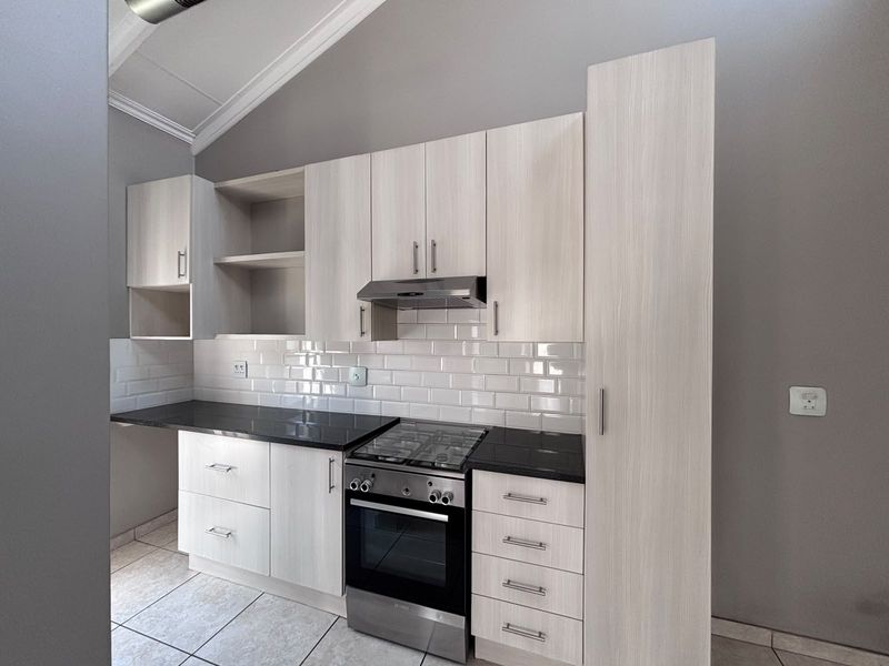 Modern kitchen featuring light wood-grain cabinetry, black stone countertops, subway tile backsplash, and integrated stainless steel appliances under a vaulted ceiling.
