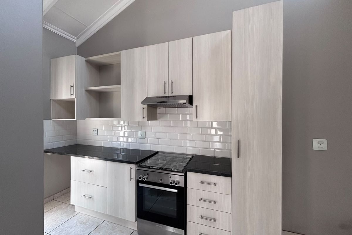 Modern kitchen featuring light wood-grain cabinetry, black stone countertops, subway tile backsplash, and integrated stainless steel appliances under a vaulted ceiling.