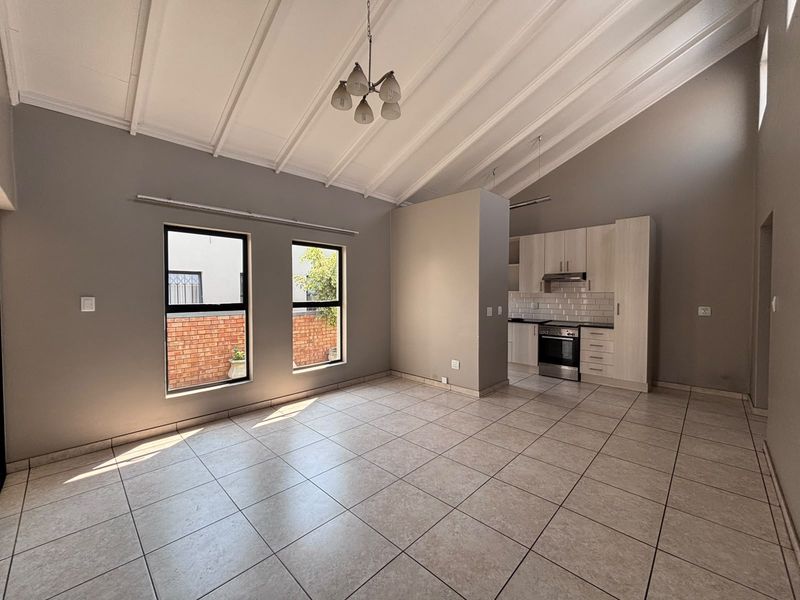 Spacious open-plan living area featuring a high vaulted ceiling, tiled flooring, and a modern kitchen with built-in cabinetry and appliances.
