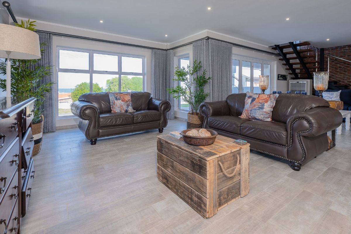 Spacious living room featuring large windows, tiled flooring, recessed lighting, and an exposed brick feature wall with an open staircase.