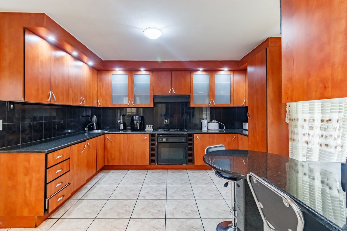 A functional kitchen featuring warm-toned wooden cabinetry, dark granite countertops, integrated appliances, and tiled flooring with ample storage space.