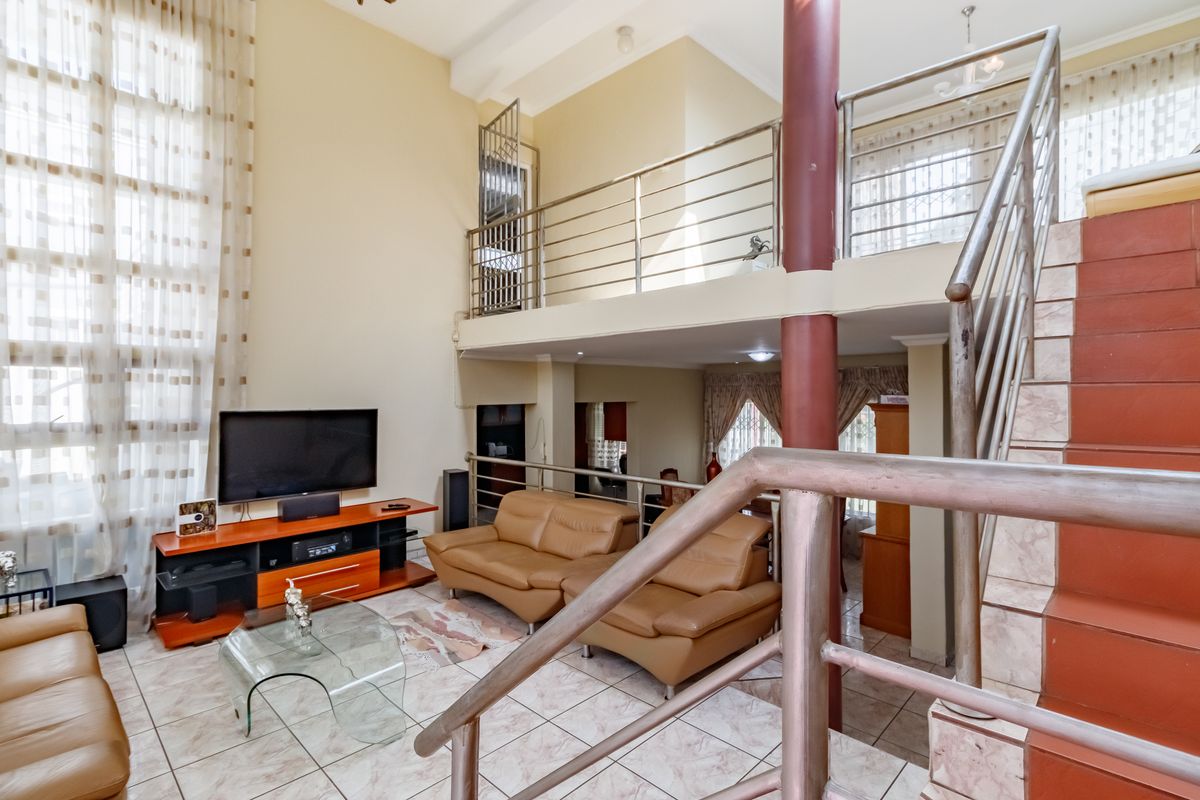 Spacious double-volume living area featuring tiled flooring, a mezzanine level with stainless steel balustrades, and an integrated staircase.