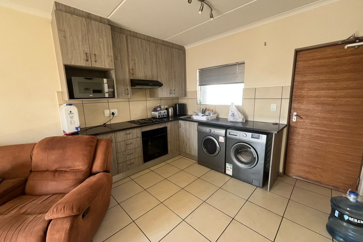 Functional kitchen featuring wood-look cabinetry, dark countertops, built-in oven and hob, tiled backsplash, and integrated laundry appliance space.