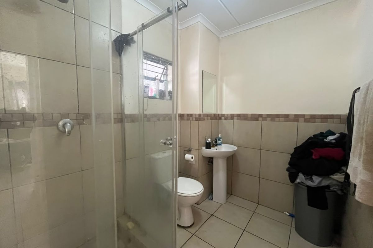 A functional bathroom featuring a shower enclosure, pedestal basin, and toilet with neutral wall and floor tiling.