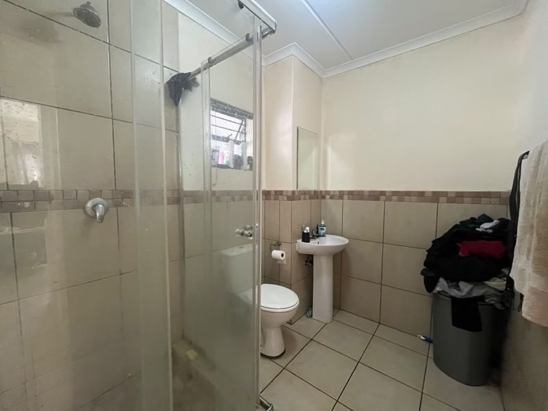 A functional bathroom featuring a shower enclosure, pedestal basin, and toilet with neutral wall and floor tiling.