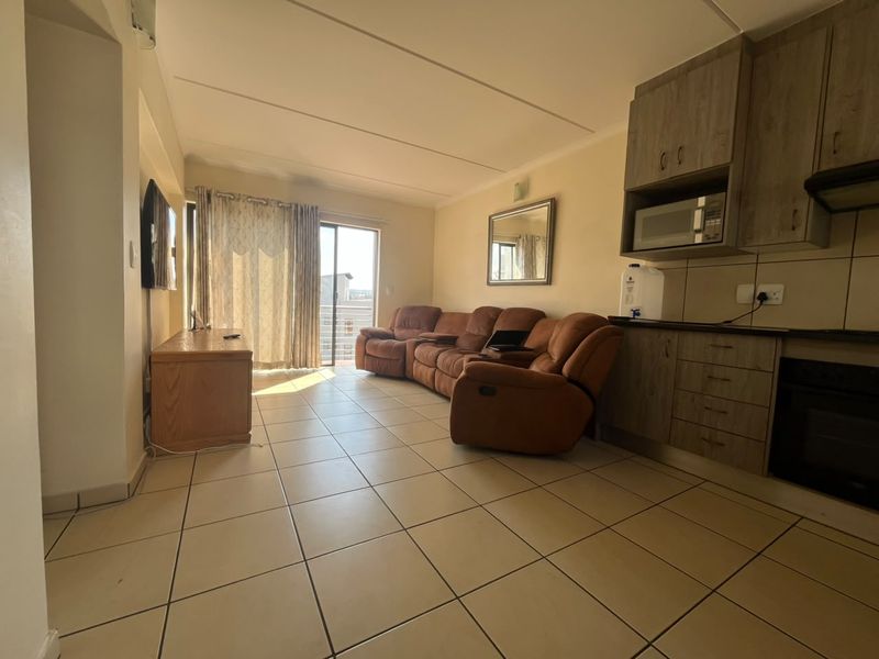 Open-plan living area featuring tiled flooring, a compact kitchen with built-in cabinetry and appliances, and direct access to a balcony through sliding doors.