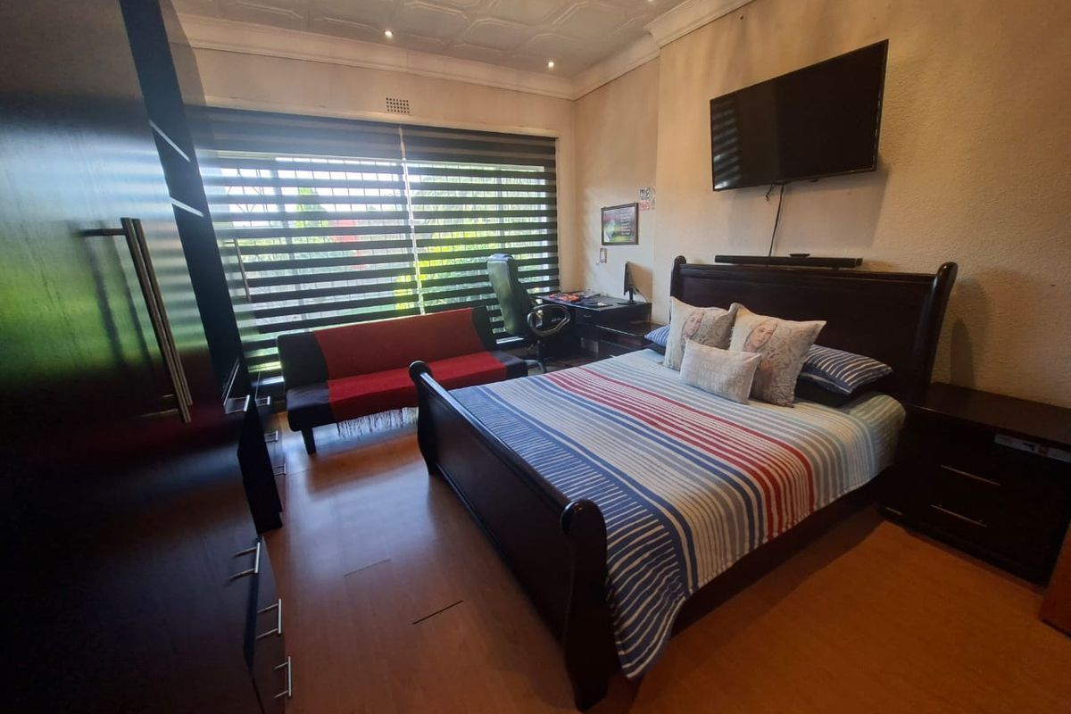 A spacious bedroom featuring laminate flooring, a decorative coffered ceiling, and large windows with fitted blinds, providing ample natural light.