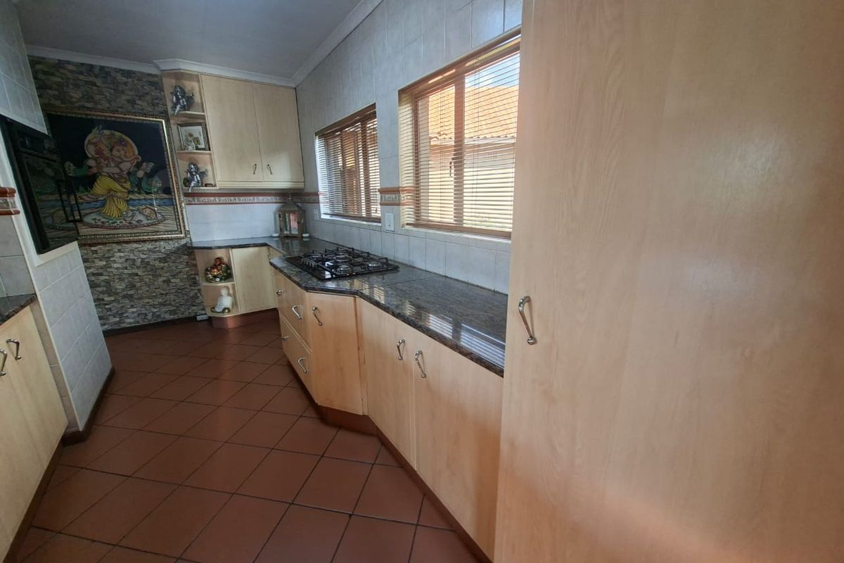 A functional kitchen featuring light wood cabinetry, granite countertops, a built-in gas hob, and tiled flooring with a decorative stone-cladding feature wall.