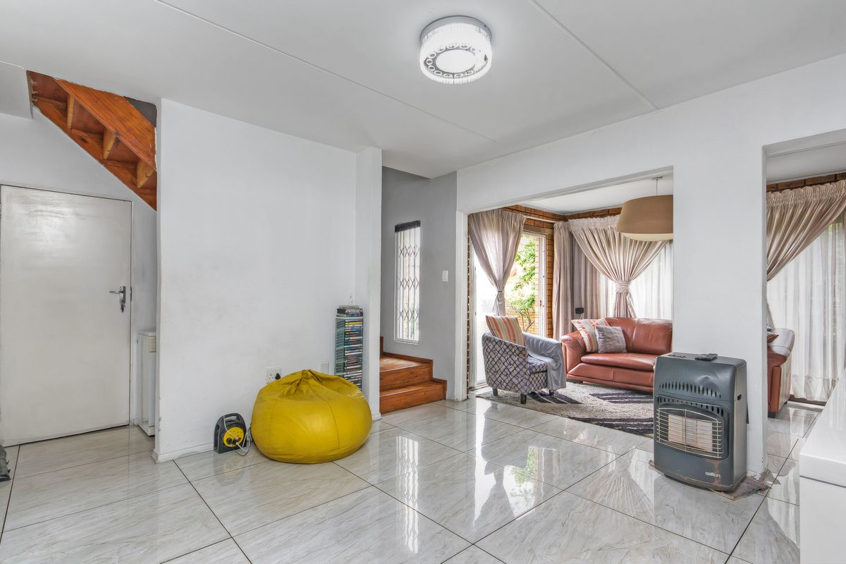 Open-plan living area featuring polished tiled flooring, a wooden staircase, and direct access to an outdoor patio through sliding glass doors.