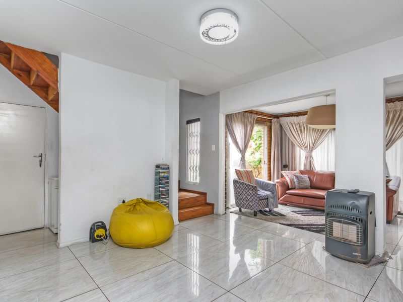 Open-plan living area featuring polished tiled flooring, a wooden staircase, and direct access to an outdoor patio through sliding glass doors.