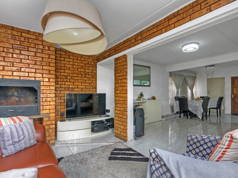 Open-plan living and dining area featuring an exposed brick wall, built-in fireplace, and polished tiled flooring throughout the connected spaces.