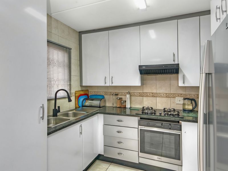 A functional kitchen featuring white cabinetry, granite countertops, a gas hob, built-in oven, and a double basin sink with a modern faucet.
