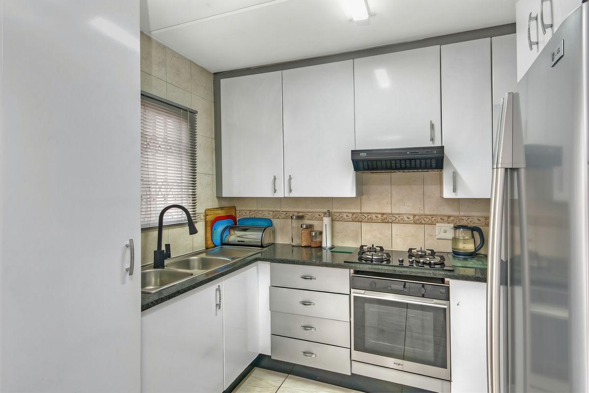 A functional kitchen featuring white cabinetry, granite countertops, a gas hob, built-in oven, and a double basin sink with a modern faucet.