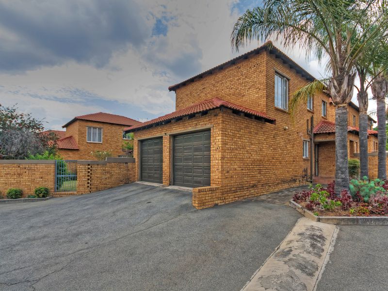 Front view of a double-story townhouse featuring a face brick exterior, tiled roof, and a double garage with a paved driveway.