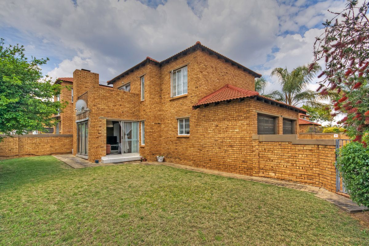 Rear view of a double-story face brick townhouse featuring a private garden, paved walkway, and integrated double garage.
