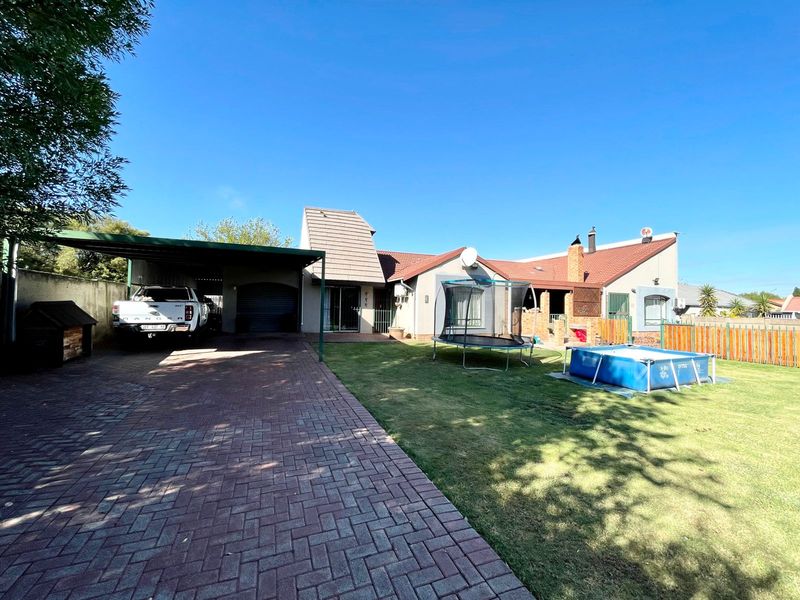 Front view of the property featuring a paved driveway, carport, tiled roof, and a spacious lawn area.