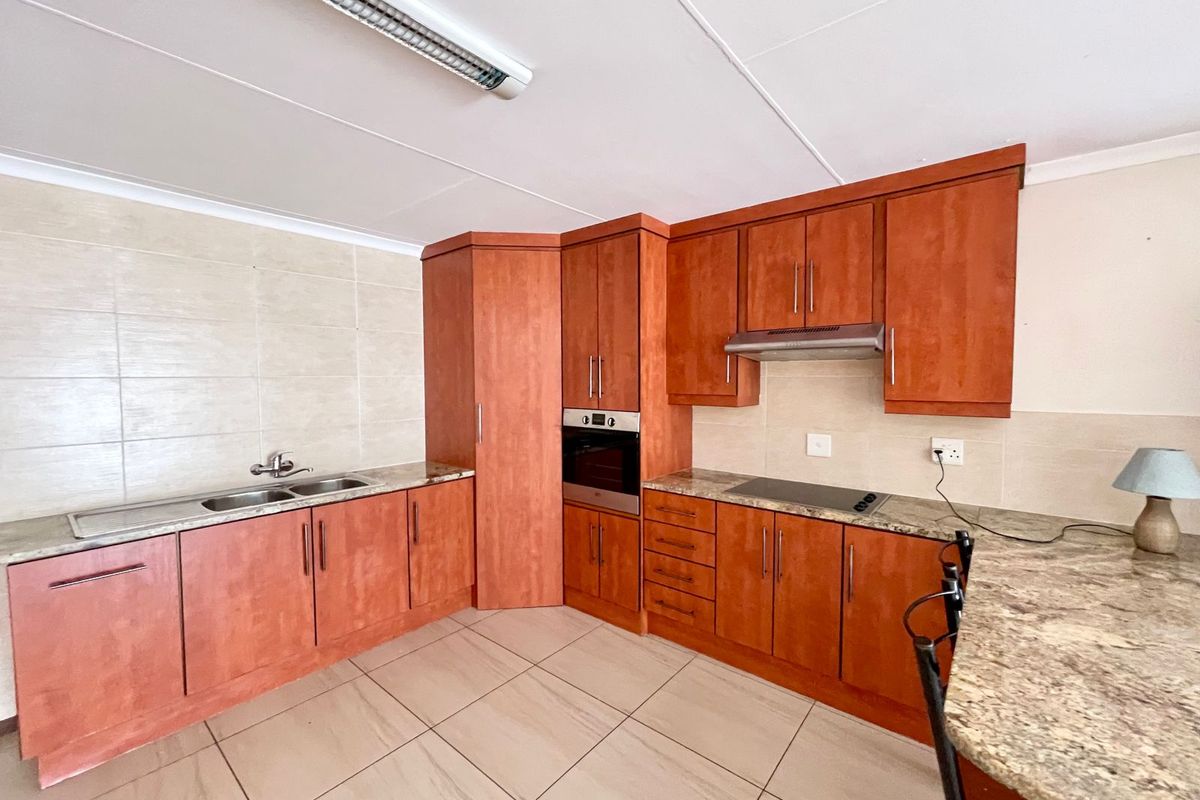 A functional kitchen featuring wood-finish cabinetry, granite countertops, built-in oven, hob, and extractor fan, complemented by neutral tiled flooring and backsplash.