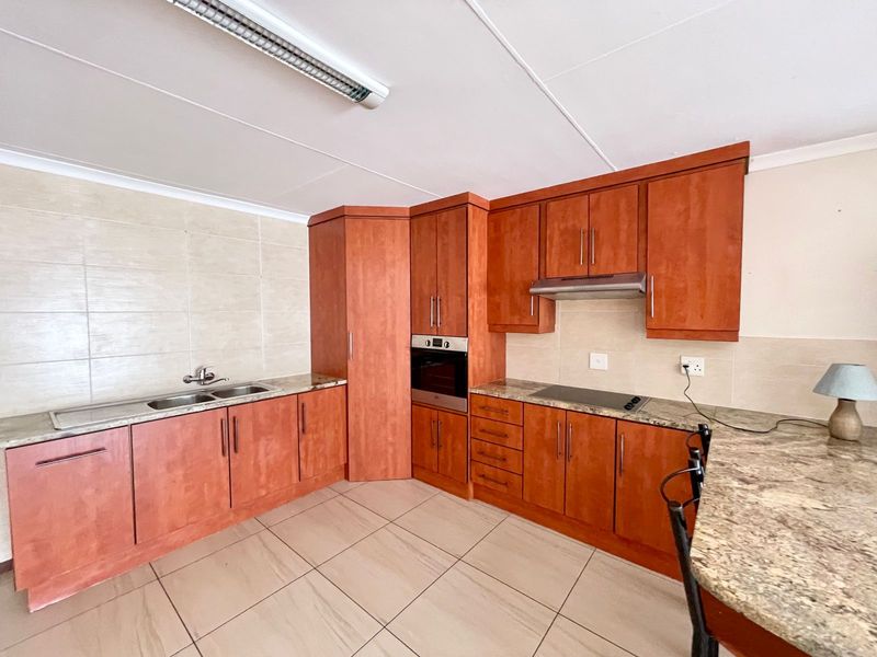 A functional kitchen featuring wood-finish cabinetry, granite countertops, built-in oven, hob, and extractor fan, complemented by neutral tiled flooring and backsplash.