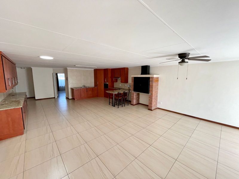 Spacious open-plan living and kitchen area featuring tiled floors, built-in cabinetry, stone countertops, and a brick fireplace.