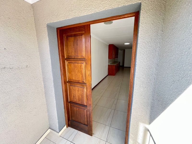 An entrance area featuring a solid wooden door leading into an open-plan living and kitchen space with tiled flooring.