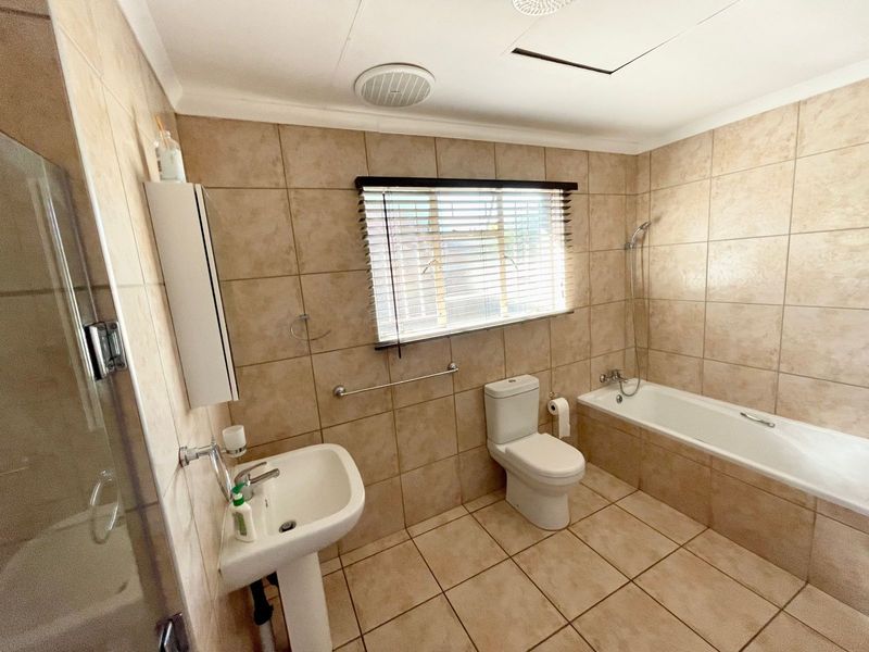 A functional bathroom featuring neutral wall and floor tiles, a pedestal basin, a toilet, and a bathtub with a handheld shower attachment.