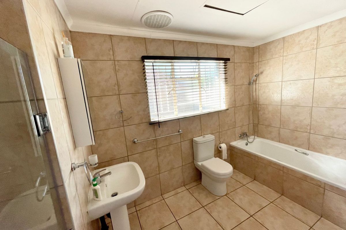 A functional bathroom featuring neutral wall and floor tiles, a pedestal basin, a toilet, and a bathtub with a handheld shower attachment.