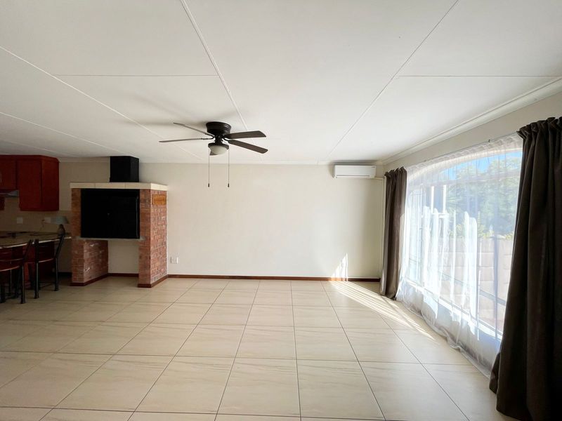 Spacious open-plan living area featuring tiled floors, a brick fireplace, ceiling fan, and split-system air conditioning, with an adjoining kitchen breakfast bar.