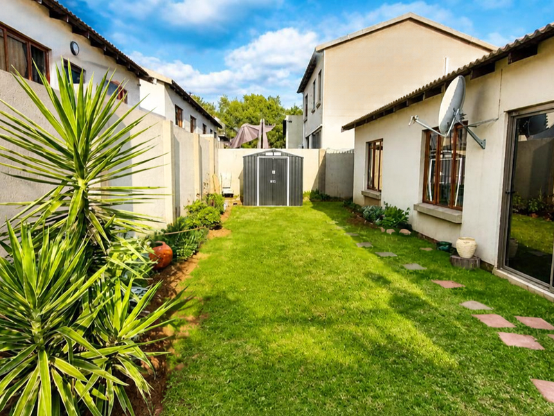 A private rear garden featuring a lawn, paved stepping stones, boundary walls, and a sliding glass door providing access to the townhouse interior.