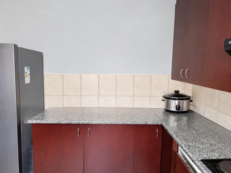 A functional kitchen area featuring dark wood cabinetry, granite countertops, a tiled backsplash, and a built-in electric hob with an extractor fan.