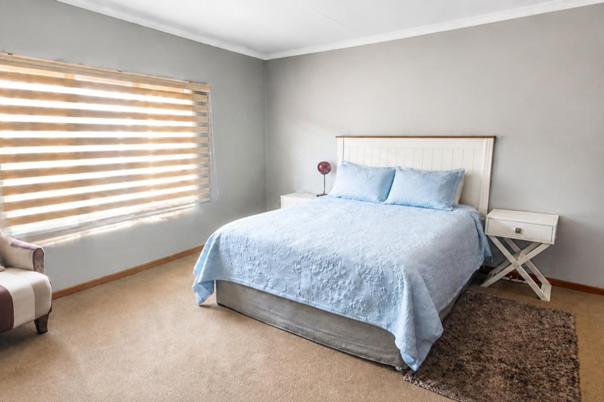 A well-maintained bedroom featuring neutral wall tones, carpeted flooring, a built-in wardrobe, and modern zebra blinds for adjustable natural light.