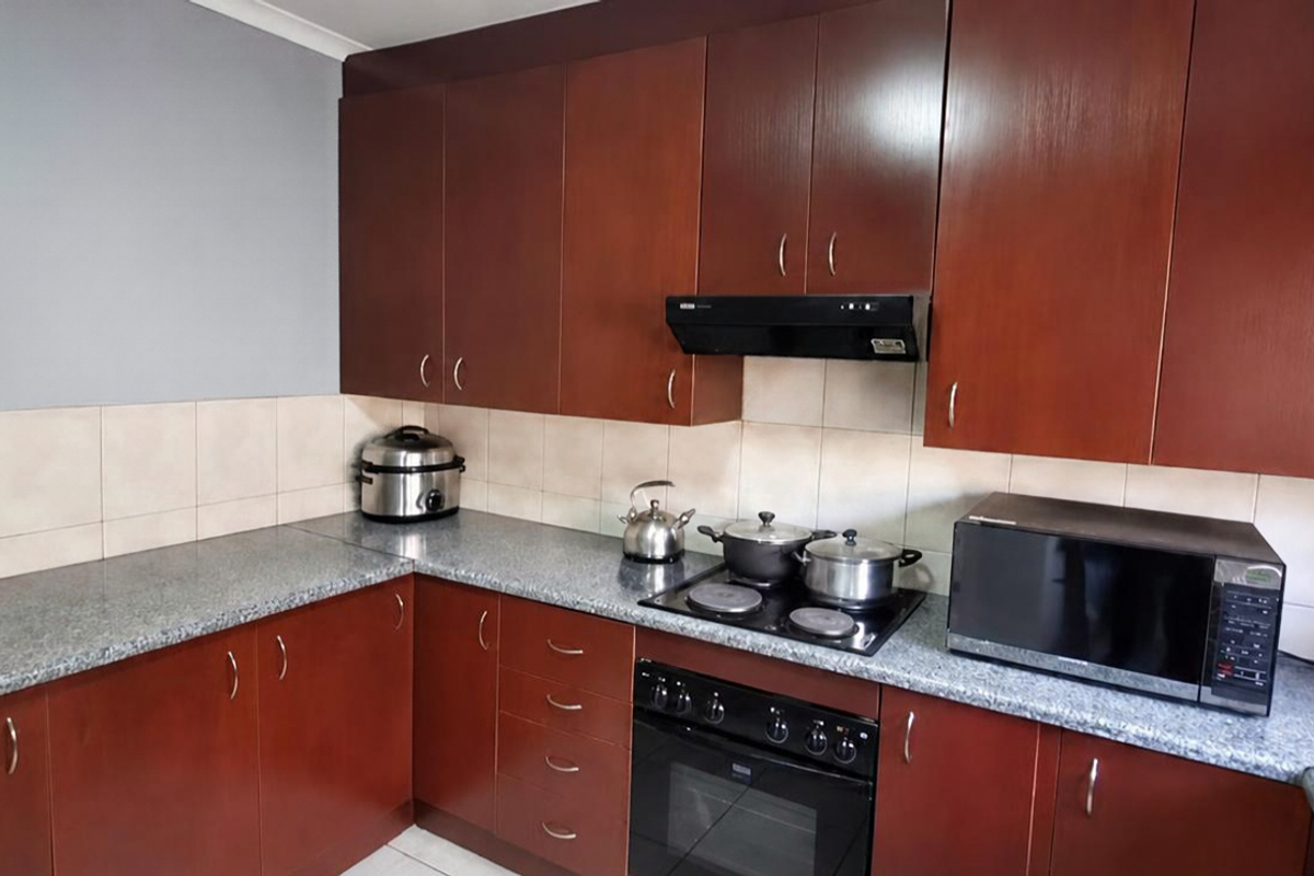 A functional kitchen featuring dark wood-look cabinetry, granite countertops, a tiled backsplash, and integrated cooking appliances including an oven and electric hob.