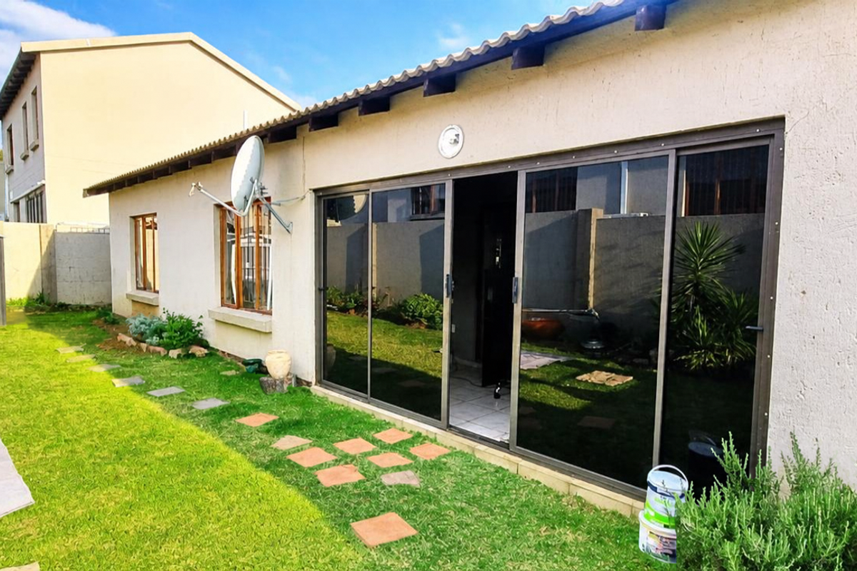 Rear view of the townhouse featuring a lawn, metal garden shed, and large sliding glass doors leading into the living area.