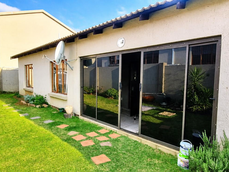 Rear view of the townhouse featuring a lawn, metal garden shed, and large sliding glass doors leading into the living area.